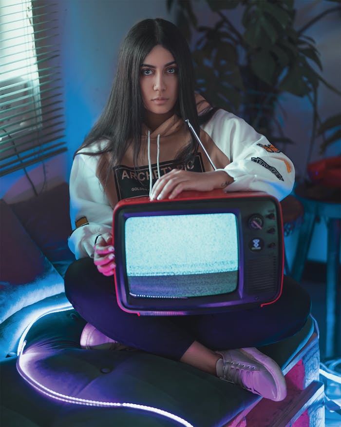Young woman with long hair holding a vintage TV with static screen in a moody, atmospheric room.